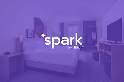 Spark by Hilton logo set on transparent purple over an image of a bedroom