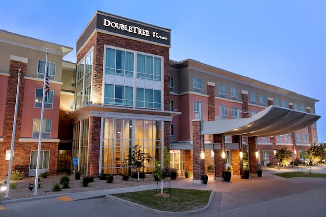 Illuminated Hotel Exterior, Signage, Porte Cochere, Flagpole, Landscaping, and Parking Lot at Dusk