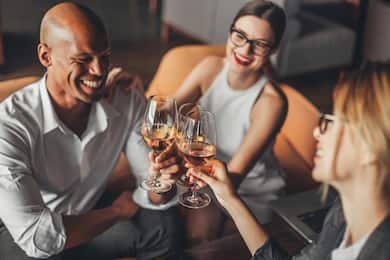 A smiling man and two women raise glasses of wine.