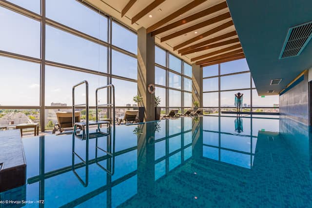 Indoor swimming pool with floor to ceiling windows and views of the city and outdoors