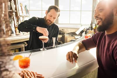 Man sitting at bar, bartender in background mixing a cocktail