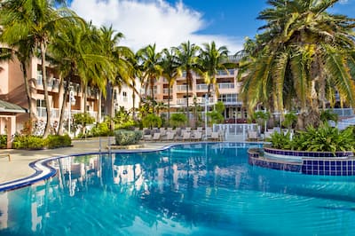 Daytime View of Outdoor Pool Area With Waterfall and Loungers Surrounded by Palm Trees and View of Guest Room Balconies