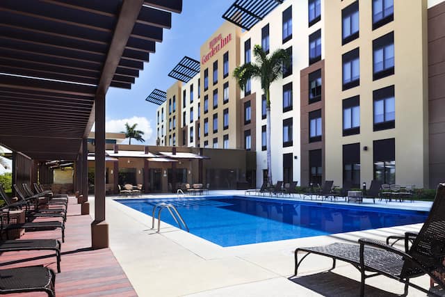 Outdoor Pool with Chaise Lounge Chairs and View of Hotel Exterior and Signage on a Sunny Day