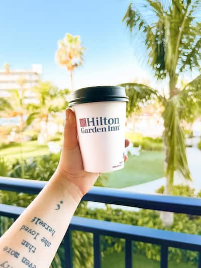 A hand holding a coffee cup with the Hilton Garden Inn logo