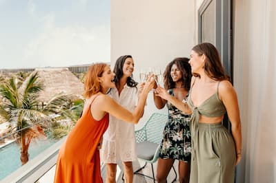 A group of four women raise a drink together on a hotel balcony