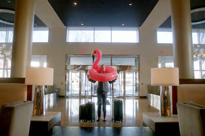 A man with a flamingo pool raft over his head in a business suit in the lobby of a hotel.