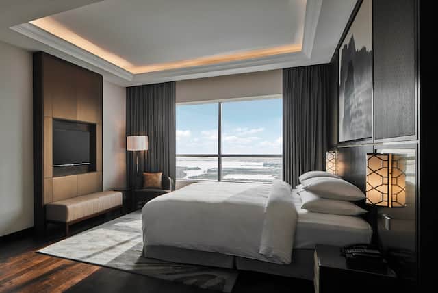Presidential suite bedroom with a king bed, a TV mounted into the wall and a large picture frame window.