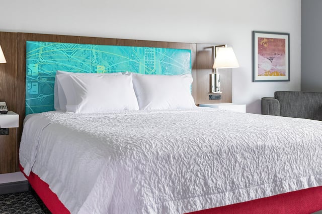 A king bed and chair in a room at a Hampton by Hilton.