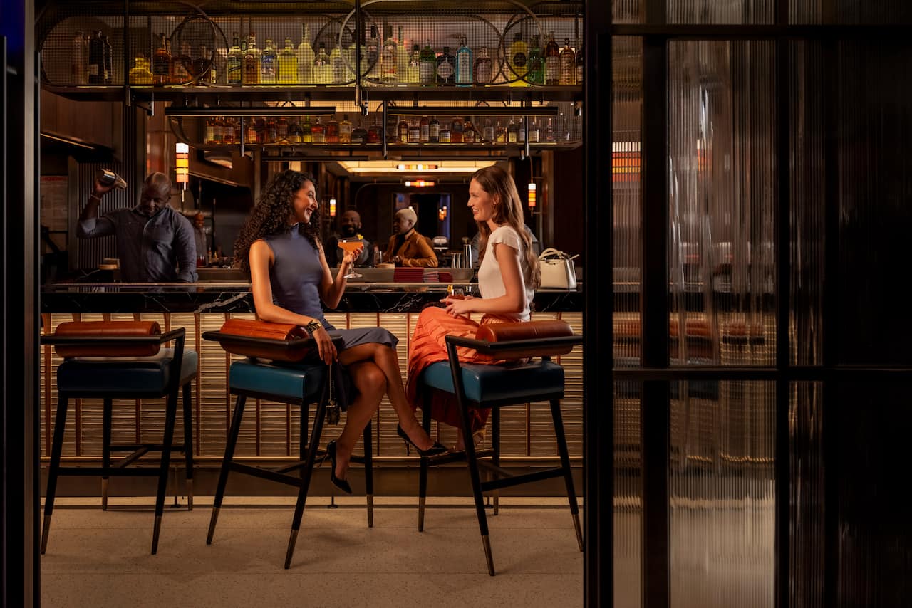 Two women drink cocktails seated at a bar