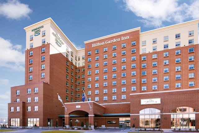 Daytime View of Hotel Exterior With Dual Branded Signage, Flagpoles, Landscaping, and Porte Cochère