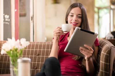 A smiling woman with a tablet computer in one hand and a cup of coffee in another