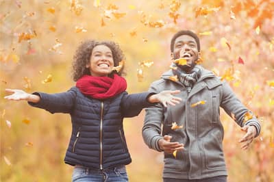Happy African American couple playing with leaves during autumn.