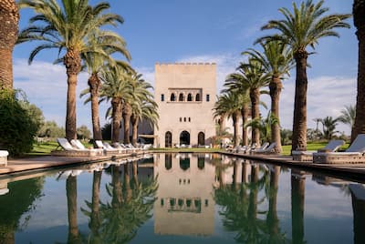 Exterior shot of the palm-tree-lined Ksar Char-Bagh reflecting off the outdoor pool