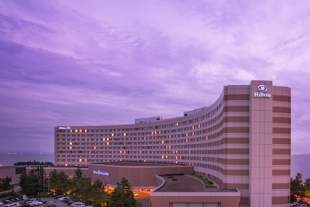 Illuminated Hotel Exterior, Signage, and Guest Cars on Parking Lot at Dusk